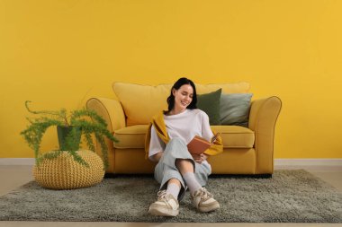 Evdeki sarı kanepenin yanında kitap okuyan güzel genç bir kadın.