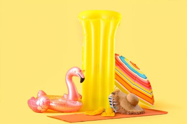 Şişme yüzük, yüzme şiltesi, güneş şemsiyesi ve sarı arka planda plaj aksesuarları. Seyahat kavramı