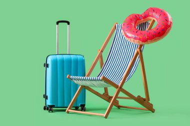 Şişirilebilir halka, güverte sandalyesi ve yeşil arka planda bavul. Seyahat kavramı