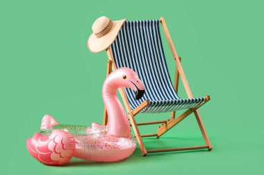 Flamingo şeklinde şişirilebilir halka ve yeşil arka planda güverte koltuğu. Seyahat kavramı