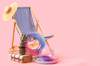 Şişirilebilir halkalar, güverte sandalyesi ve pembe arka planda ananas ve güneş gözlüğü olan bavul. Seyahat kavramı