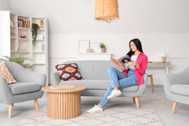 Gözlüklü genç kadın evdeki kanepede dergi okuyor.