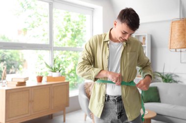 Genç adam evde belini ölçüyor. Kilo verme konsepti