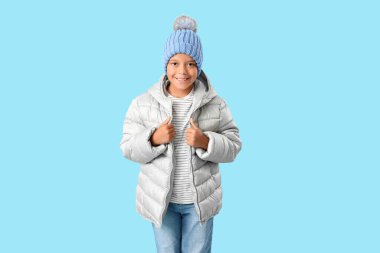 Mavi arka planda kışlık giysiler içinde şirin, mutlu, Afro-Amerikalı bir çocuk.