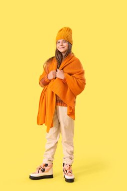 Sarı arka planda kışlık giysiler içinde şirin, şık, mutlu bir kız.