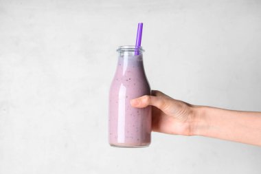 Beyaz arka planda bir şişe taze leylak içeceği olan bir kadın eli.