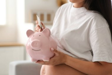 Genç hamile kadın evdeki domuz kumbarasına para yatırıyor, yakın plan. Annelik Faydası konsepti