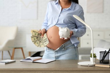 Domuz kumbarası ve evde parası olan genç hamile bir kadın, yakın plan. Annelik Faydası konsepti