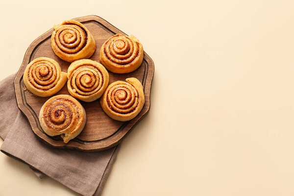 Board with tasty cinnamon rolls on light background