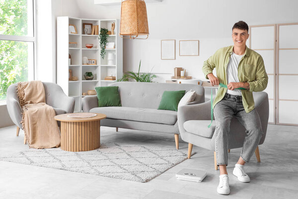 Молодой человек измеряет талию дома. Концепция потери веса