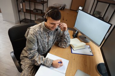 Merkezde bilgisayar ve günlükle çalışan kulaklıklı genç bir asker.