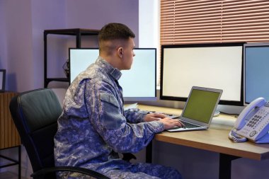 Genç erkek asker geceleri merkezde dizüstü bilgisayarla çalışıyor.
