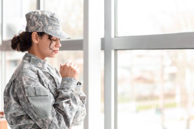 Kadın Afro-Amerikalı asker karargahın penceresinin yanında dua ediyor.