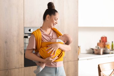 Mutfakta askısında küçük sevimli bir bebekle genç mutlu bir anne.