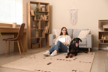 Tatlı Doberman köpeği ve evde dizüstü bilgisayarı olan güzel, mutlu bir kadın.