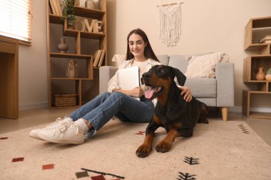 Tatlı Doberman köpeği ve evde dizüstü bilgisayarı olan güzel, mutlu bir kadın.