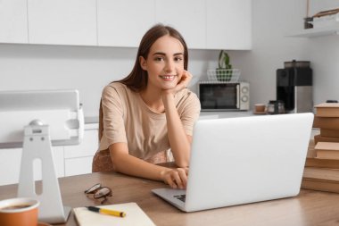 Mutfakta bilgisayar, tablet ve kitap okuyan mutlu bir kız öğrenci.