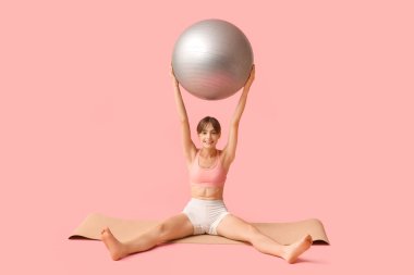 Pembe arka planda fitball oynayan genç bir kadın.