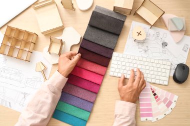 Kumaş örnekleri ve bilgisayar ile ahşap masa üzerinde çalışan erkek mobilya tasarımcısı, üst görünüm