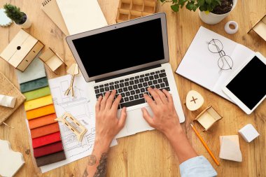 Erkek mobilya tasarımcısı dizüstü bilgisayarla ahşap masada çalışıyor.