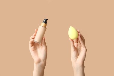 Makyaj malzemesi şişesi ve kahverengi arka planda süngeri olan kadın elleri.