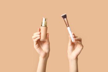 Makyaj malzemesi şişesi ve kahverengi arka planda fırçası olan kadın elleri.