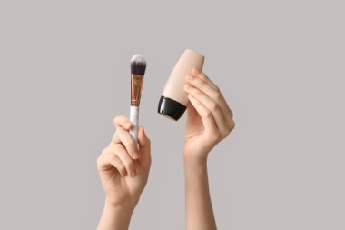 Makyaj malzemesi tübü olan kadın elleri ve gri arka planda fırça