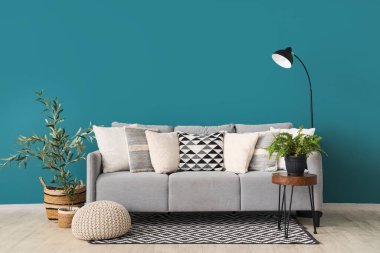 Yastıklı, çiçekli ve mavi duvarlı şık gri kanepe.