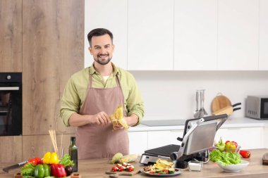 Mutfaktaki modern elektrikli ızgarada mısır koçanı soyan genç adam.