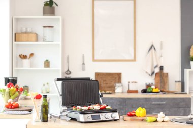 Mutfaktaki masada taze sebzelerle modern elektrikli ızgara.