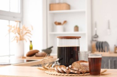 Kavanoz dolusu lezzetli kvass, bardaklar, ekmek dilimleri ve mutfaktaki masada dikenler.