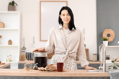 Mutfakta bir kavanoz lezzetli kvass, ekmek dilimleri ve dikenleri olan mutlu genç bir kadın.
