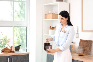 Ekmek ve dikenleri olan genç bir kadın mutfaktaki cama lezzetli kvass döküyor.