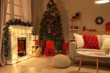 Geceleri oturma odasının içinde Noel ağacı, kanepe ve parlayan lamba var.