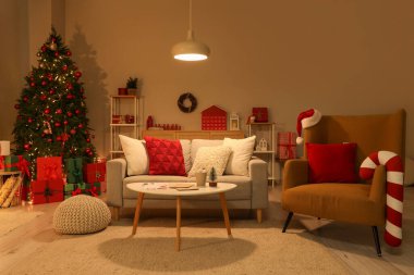 Geceleri oturma odasının içinde Noel ağacı, kanepe ve parlayan lamba var.