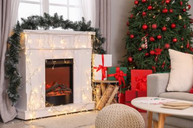 Oturma odasının içinde Noel ağacı, şömine ve parlayan ışıklar var.