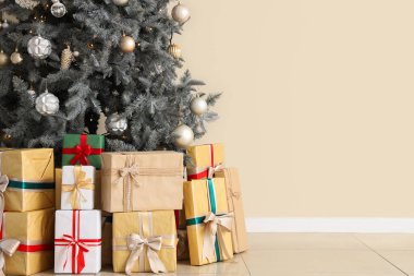 Bej duvarın yanında hediyeleri olan Noel ağacı.