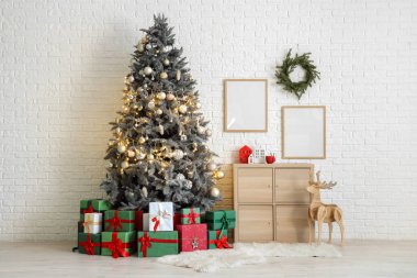 Noel ağacı hediye kutuları, şenlikli dekorasyonlar ve beyaz tuğla duvarın yanındaki ahşap dolap.