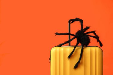 Suitcase with Halloween decoration spider on orange background clipart