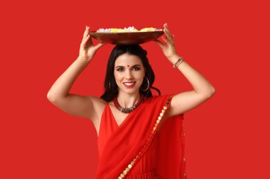 Sari giymiş, elinde mumlar ve kırmızı arka planda çiçeklerle güzel, mutlu bir Hintli kadın. Divaly kutlaması