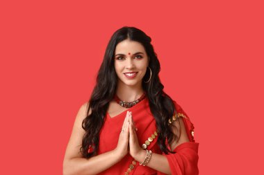 Geleneksel sari giymiş güzel, genç, mutlu bir Hintli kadın kırmızı arka planda dua ediyor. Divaly kutlaması