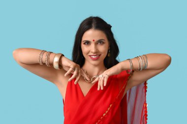 Beautiful young happy Indian woman in traditional sari dancing on blue background. Divaly celebration clipart