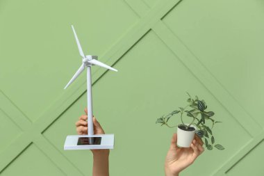 Rüzgâr türbini modeline sahip kadın eller ve renkli arka planda bitki. Yeşil enerji kavramı