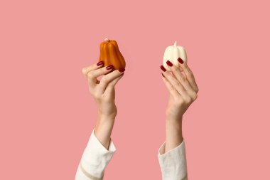 Pembe arka planda balkabağı şeklinde sonbahar mumları olan kadın eller.