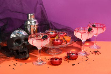 Mor arka planda turuncu masada Cadılar Bayramı dekoru olan kokteyller