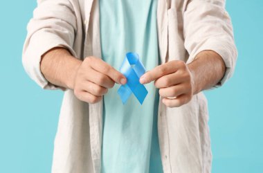 Renkli arka planda mavi kurdeleli genç adam, yakın plan. Prostat kanseri farkındalığı