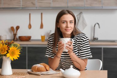 Mutfaktaki masada çay içen genç bir kadın.