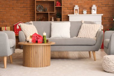 Oturma odasındaki masada ev şeklinde tutacakları ve Noel dekoru olan mumlar yakmak.