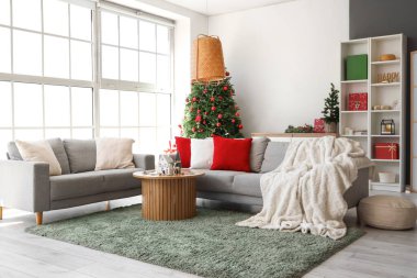 Oturma odasının içinde Noel ağaçları, kanepeler ve mum tutacakları var.