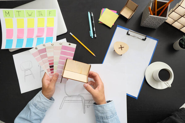 Дизайнер мужской мебели с цветовыми палитрами и миниатюрной моделью, работающей на черном столе, вид сверху